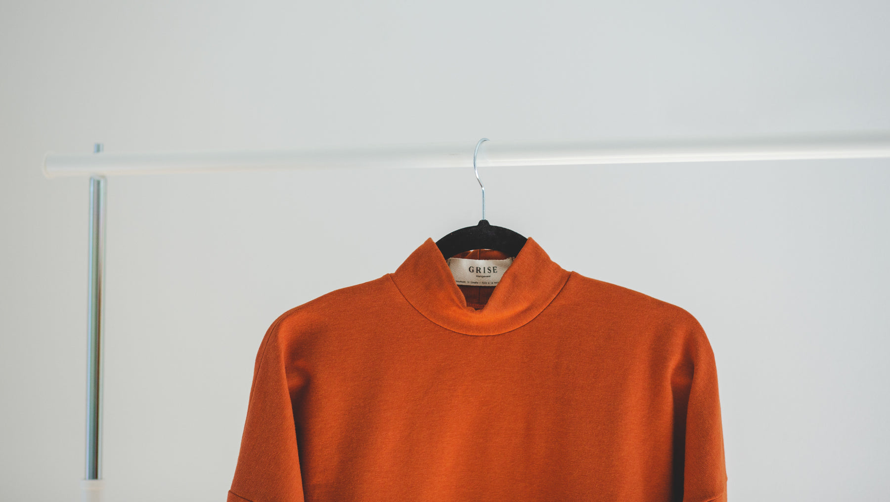 Grise Loungewear sweater in orange or ginger color hanging on a garment support